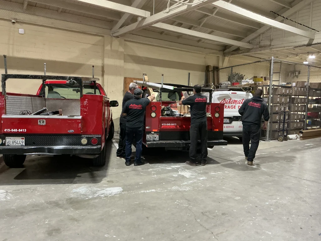 A team of Certified Garage Door Technicians in San Francisco loading equipment onto service trucks inside a warehouse.