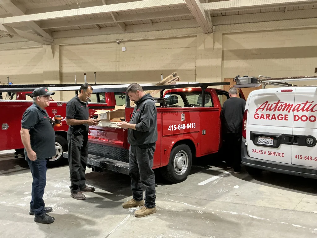 A team of service technicians gathering around work trucks inside a warehouse, representing local Garage Door Experts in San Francisco.