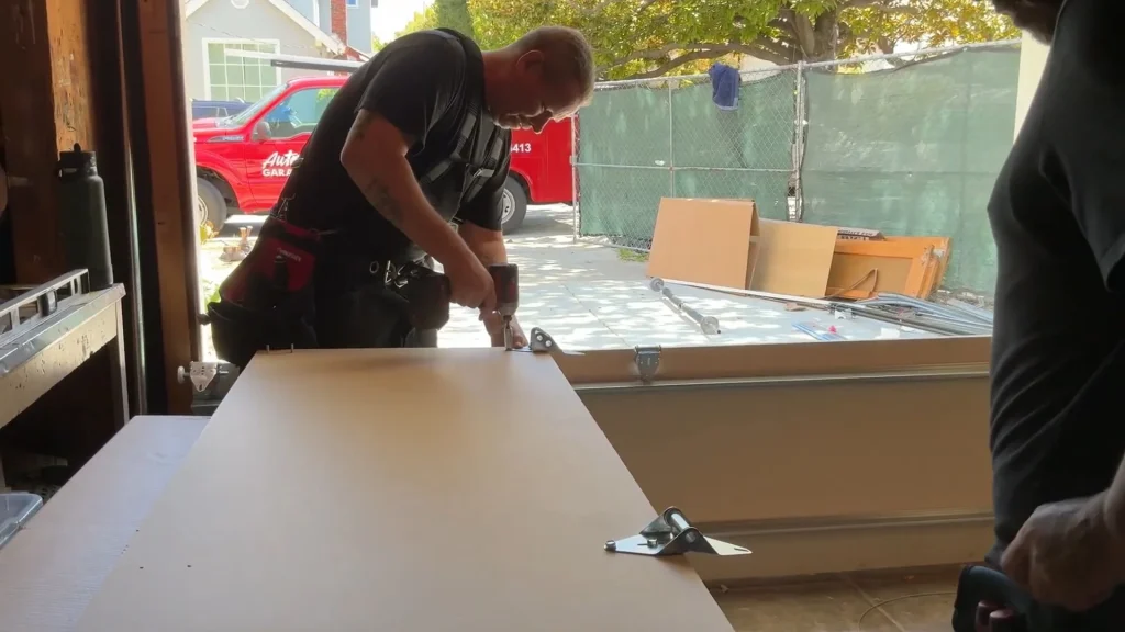 A skilled technician using a power tool to fasten hardware onto a door section panel during a Professional Garage Door Repair project.