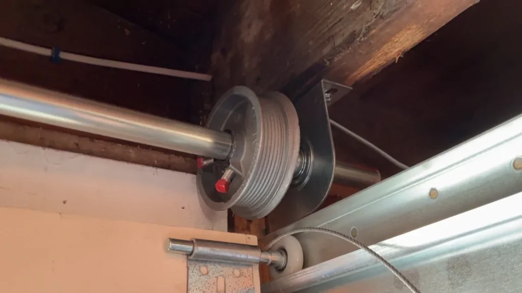 Close-up of a metal drum pulley and high-tension steel Garage Door Cables attached near the top corner track.