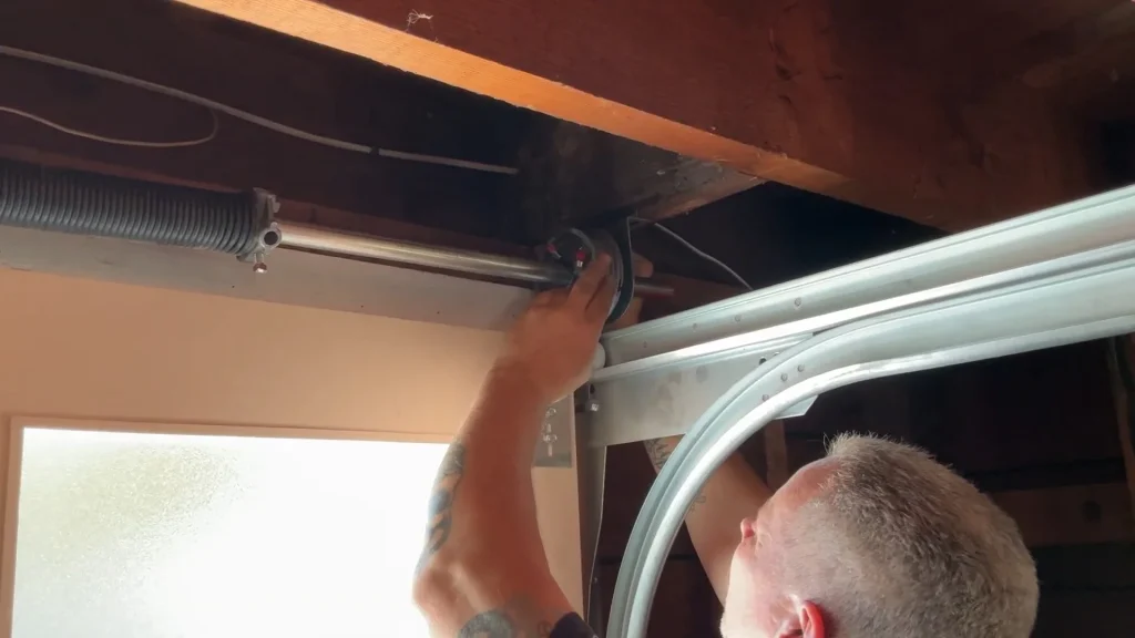 A technician reaching up to guide and attach wire onto a drum pulley during a garage door cable replacement in San Francisco, CA.