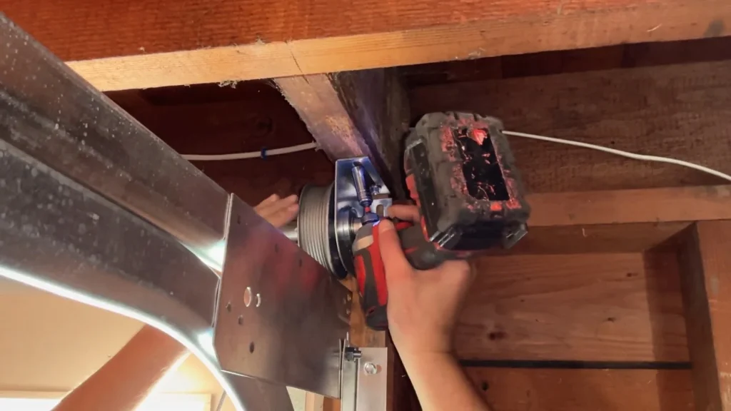 A technician using a power tool to adjust the cable drum bracket during a process to replace garage door cables.