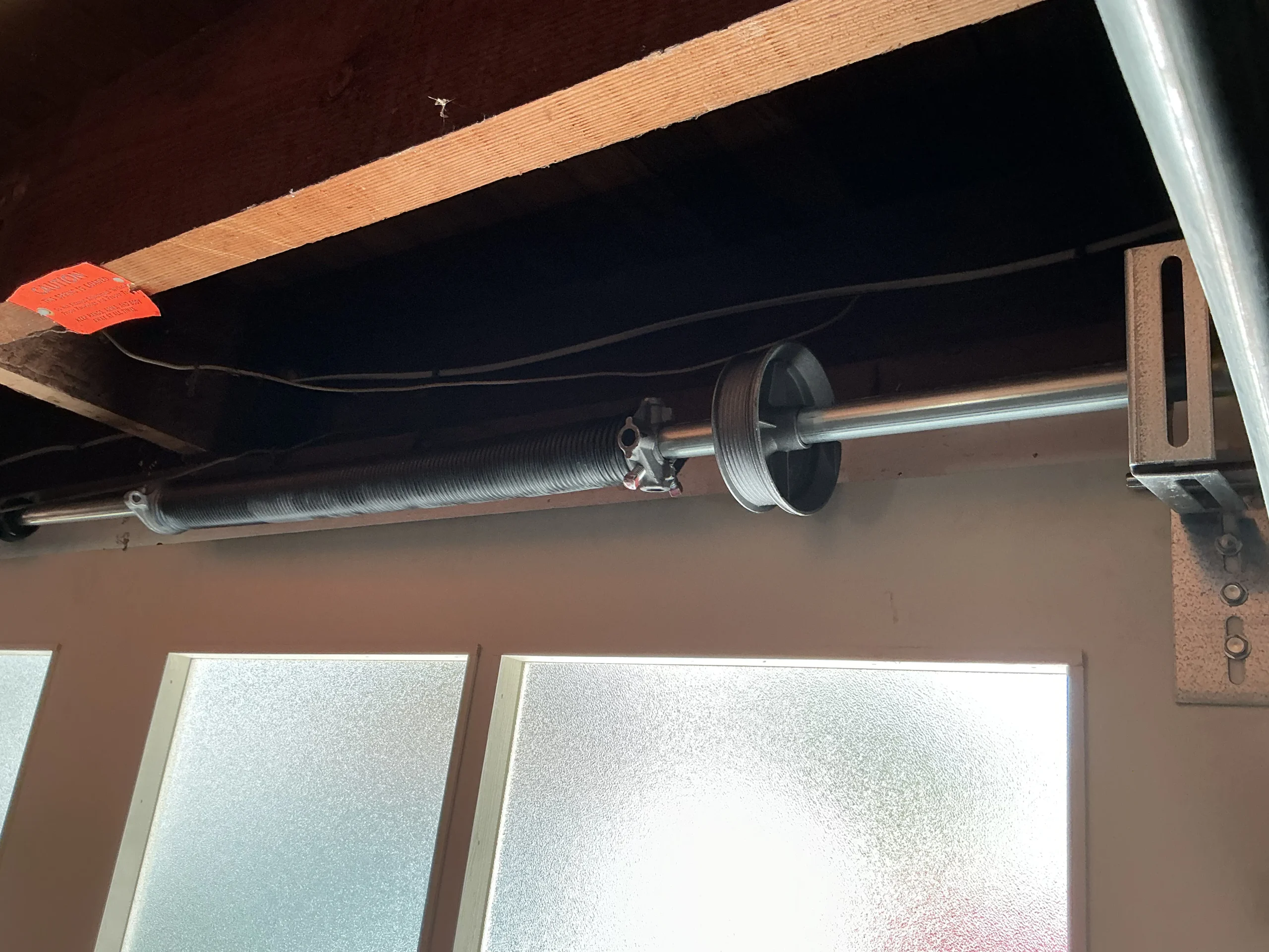 A close-up view of an overhead torsion assembly and cable drum above garage door windows, inspected as part of a Garage Door Spring Tune-Up.