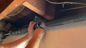 A close-up view of hands working under wooden rafters to align and service an overhead coil, showing maintenance to address what causes a garage door spring to break.