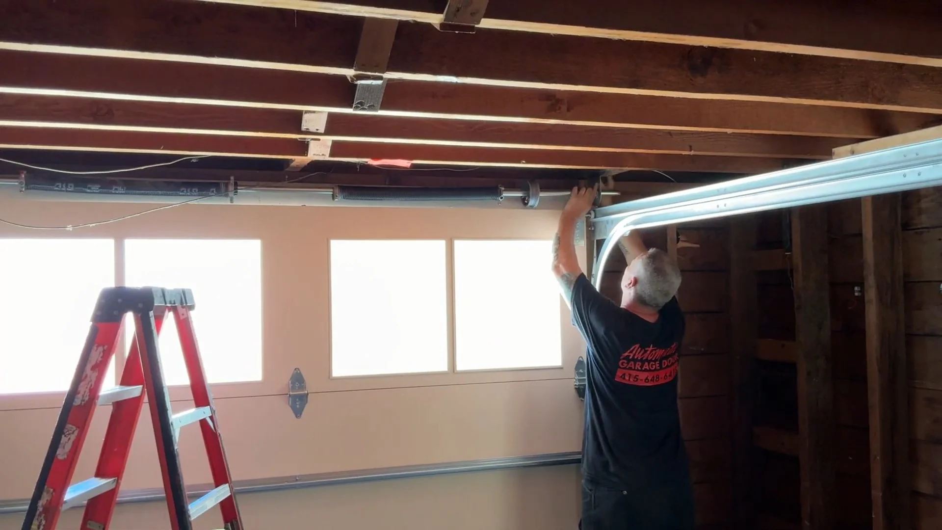 A technician working overhead near garage door windows to provide Professional Garage Door Spring Repair in San Francisco.
