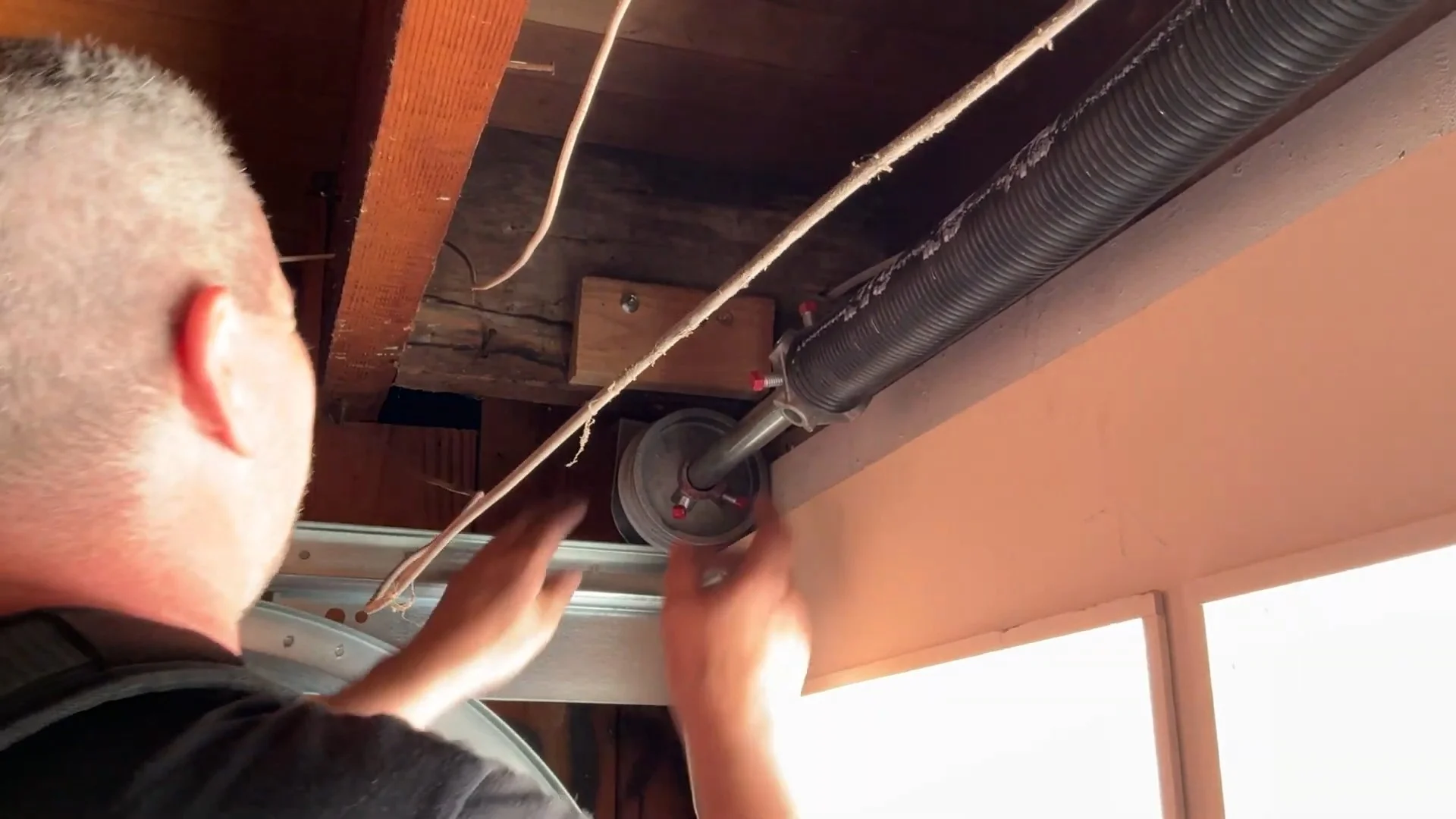 A technician working overhead on a high-tension torsion mechanism to perform a garage door spring repair in San Francisco, CA